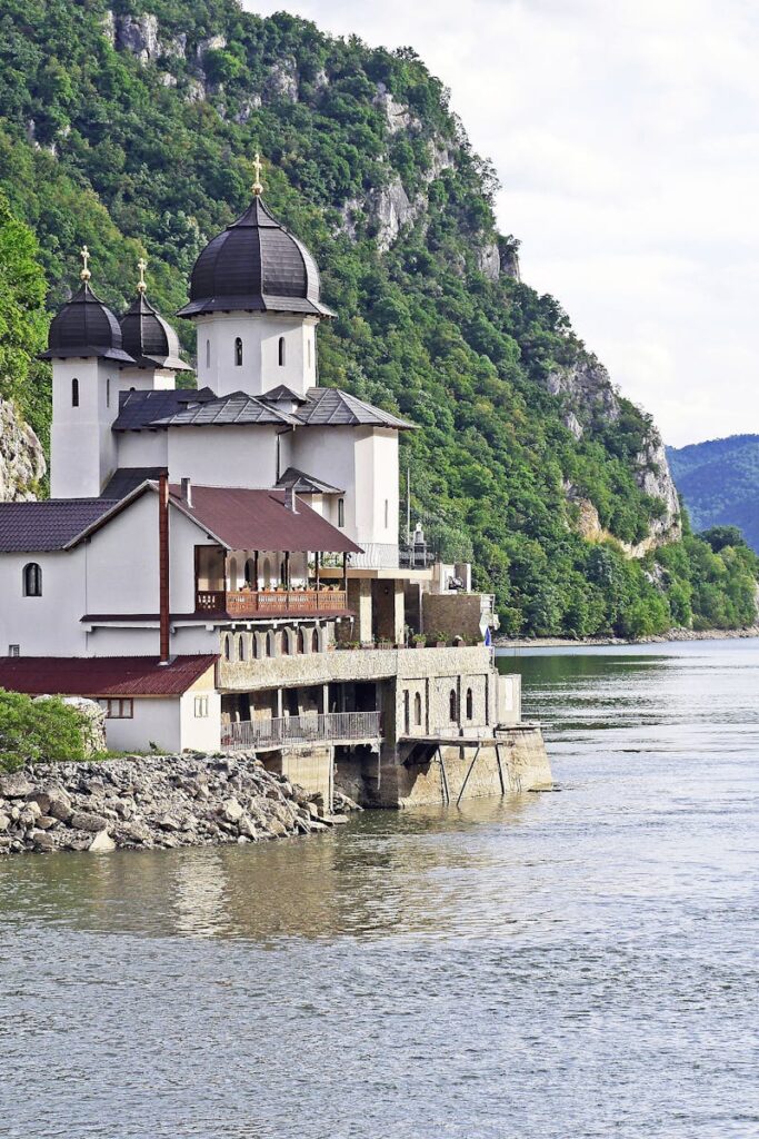 Scenic Orthodox monastery by the Danube River gorge in summer, set against lush green mountains.